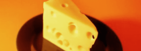 Image: A close-up of a piece of Swiss cheese with holes, dramatically lit against an orange background, creating a warm, vibrant atmosphere. -- D.C. Douglas