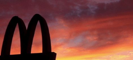 Image: Silhouette of the McDonald's golden arches against a vibrant orange and red sunset sky that sizzles with color. -- D.C. Douglas