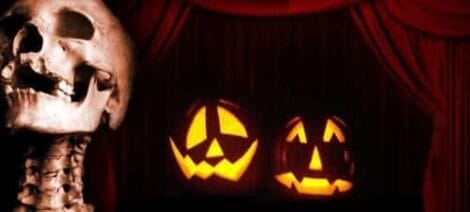 Image: A spooky halloween themed image featuring a human skull on the left with two carved glowing jack-o'-lanterns in the background, set against a backdrop of "My Bloody" red curtains. -- D.C. Douglas