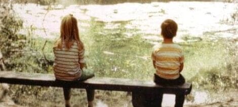 Image: Two children, wearing matching striped shirts, sit on a bench overlooking a serene pond covered with lily pads on Mother's Day. -- D.C. Douglas