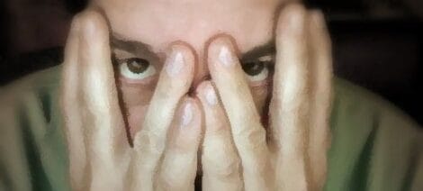 Image: A person peering through fingers covering their face, expressing stress or worry during actor auditions, with a softly blurred background enhancing the focus on their eyes. -- D.C. Douglas