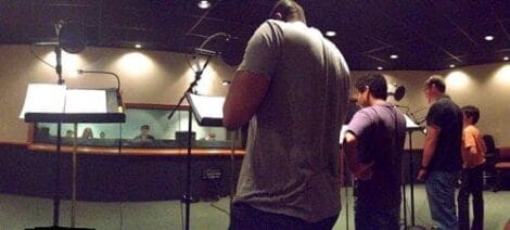 Image: Voice actors stand before microphones in a recording studio, engaged in voice acting, with sound engineers observing from behind a glass window. -- D.C. Douglas