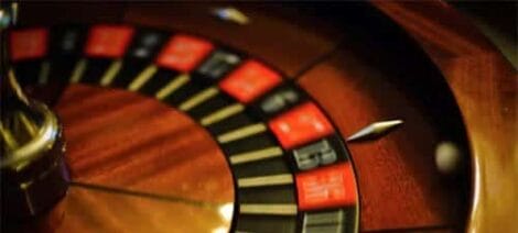 Image: Close-up of a Hollywood Roulette wheel with focus on red and black numbers, capturing the gleam of the spinning wheel in a dimly lit setting. -- D.C. Douglas