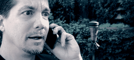 Image: A surprised man talks on his mobile phone in a garden, his eyes wide and expression shocked. The image has a cool, blue-toned filter and evokes the excitement of "Rescue Bots -- D.C. Douglas