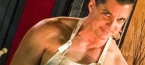 Image: Close-up of a smiling man wearing an apron, looking directly at the camera with a mischievous expression, in a warmly lit indoor setting reminiscent of TV memories. -- D.C. Douglas
