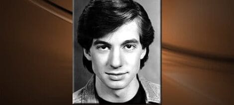Image: Black and white portrait of a young man with dark hair, wearing a denim jacket, set against a softly blurred background that transitions from dark to "Out With The Old..." light. -- D.C. Douglas
