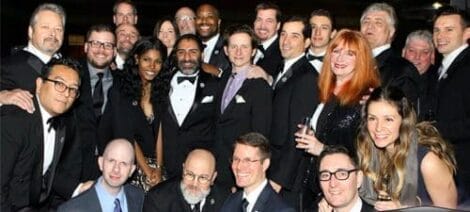Image: A group of people in formal attire posing for a photo at the Annie Awards, with smiles and varied expressions, including some standing and others seated in the front row. -- D.C. Douglas