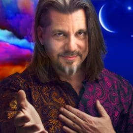 Image: A man with long brown hair and a goatee extends his hands forward, smiling. He wears a colorful paisley shirt. Abstract colorful and celestial backgrounds, including moons and clouds, surround him. -- D.C. Douglas