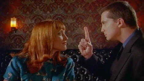 A man and a woman facing each other, with the man raising a finger while speaking.