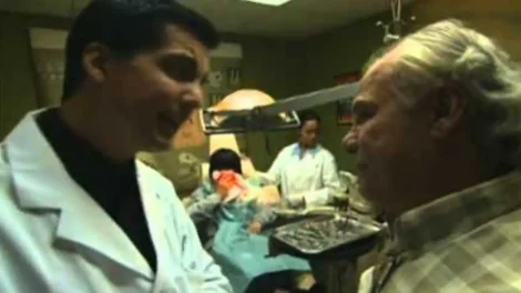 Two doctors discussing in a medical room with patients and staff in the background.
