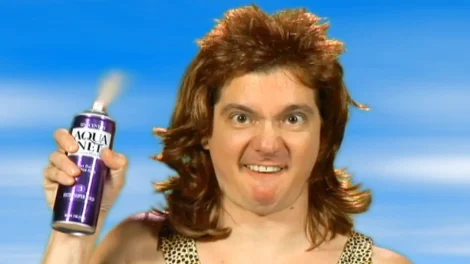 Man with a mullet hairstyle holding a can of hair spray with a serious expression.