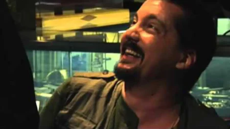 A man with a beard and short hair smiling while seated in a casual environment.