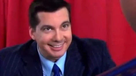 A man in a blue suit with a striped pattern smiling at another person off-camera.