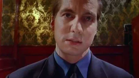 A man wearing a suit and tie with a serious expression, looking directly at the camera.