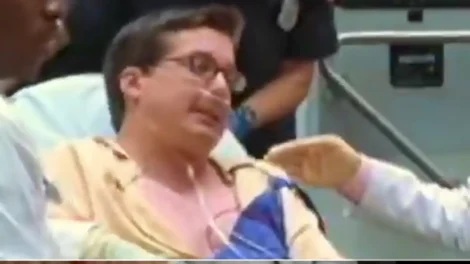 A patient in a hospital gown receiving care from medical staff in a clinical setting.