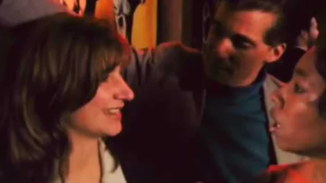 Three individuals interacting in a social setting, with one woman smiling and two men engaged in conversation.