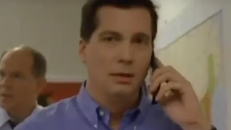 Man wearing a blue shirt talking on a mobile phone in an office environment.