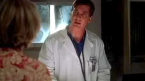 A doctor wearing a white coat speaking to a patient in a medical environment.