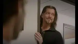 Man with long hair and a beard smiling while leaning against a door frame in an office.