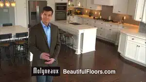 A man standing in a modern kitchen with hardwood floors and white cabinetry.