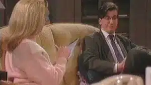 A man in a suit and a woman in a pink sweater engaged in conversation while seated.