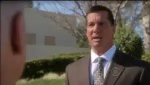 Man in a dark suit and patterned tie speaking outdoors in a clear setting.
