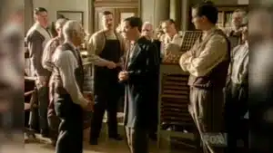 A group of men in a vintage printing shop, some shaking hands and others observing.