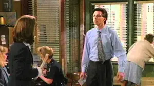 Two characters engaged in conversation in an office setting with a third person in the background.