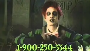 A character with red hair and dark makeup wearing a green striped shirt and bow tie, speaking directly to the camera.