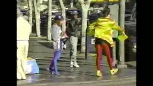 Two individuals wearing colorful outfits, one in yellow and red, and another in blue and gray, on a city street.