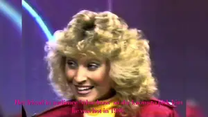 Woman with curly blonde hair wearing a red outfit, smiling and speaking during an interview.