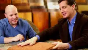 Two men seated at a table examining a sample material with a focused expression.