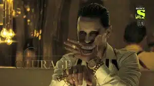 Man wearing face paint and jewelry, posing with hands in a theatrical manner.