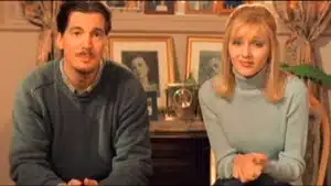 A man and woman sitting on a couch with framed pictures in the background.