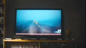 Television showing a news broadcast with a view of a road and a news ticker at the bottom.
