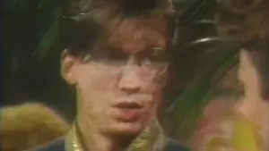 Individual wearing glasses engaged in a conversation with another person, with a blurred background.