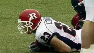 Football player wearing a red helmet and white jersey lying on the field with a football.