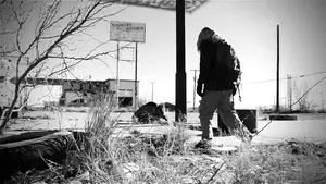 Individual walking through an abandoned area with overgrown vegetation and dilapidated structures.