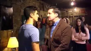 Two men facing each other in a serious discussion, with a group of people in the background.