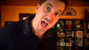 A man with an open mouth making a facial expression, wearing a dark shirt.