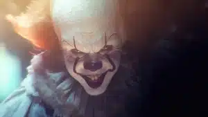 Close-up of a clown with a white face, red hair, and dark makeup around the eyes and mouth.