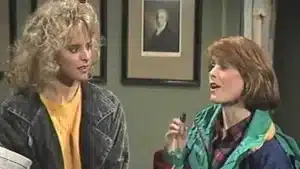 Two women talking in an indoor setting, one holding a pen and gesturing while the other listens.