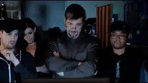 Four individuals, two men and two women, observing a screen with focused expressions in a dimly lit room.