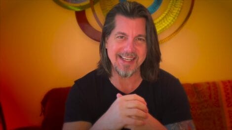 Gadfly: Breaking News &Amp; Tweaked Nipples | D.c. Douglas Man with long hair and a beard smiling while seated in front of colorful wall decorations.