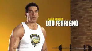 Lou Ferrigno wearing a white tank top with a fitness logo, standing next to a barbell.