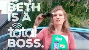 Top 5 Best Commercials Of 2025 | D.c. Douglas Woman with long hair holding sunglasses and a brochure while standing next to a car.