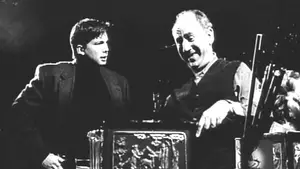 Two men engaged in conversation, one smiling and gesturing, in a black and white image.