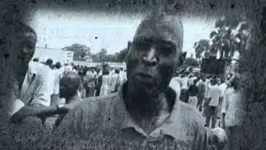 A black and white portrait of a man with a serious expression in a crowd of people.