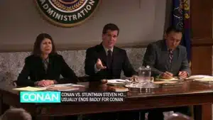 Three individuals seated at a table during a meeting, with one person gesturing while others listen.