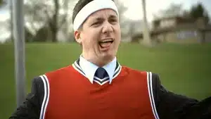 Man wearing a red sports jersey and headband, making a facial expression while standing outdoors.